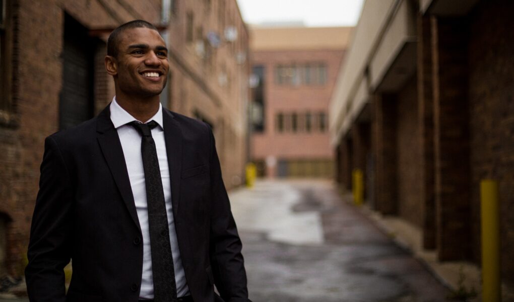 smiling man standing between brown concrete buildings at daytime