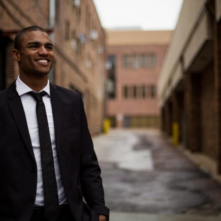 smiling man standing between brown concrete buildings at daytime